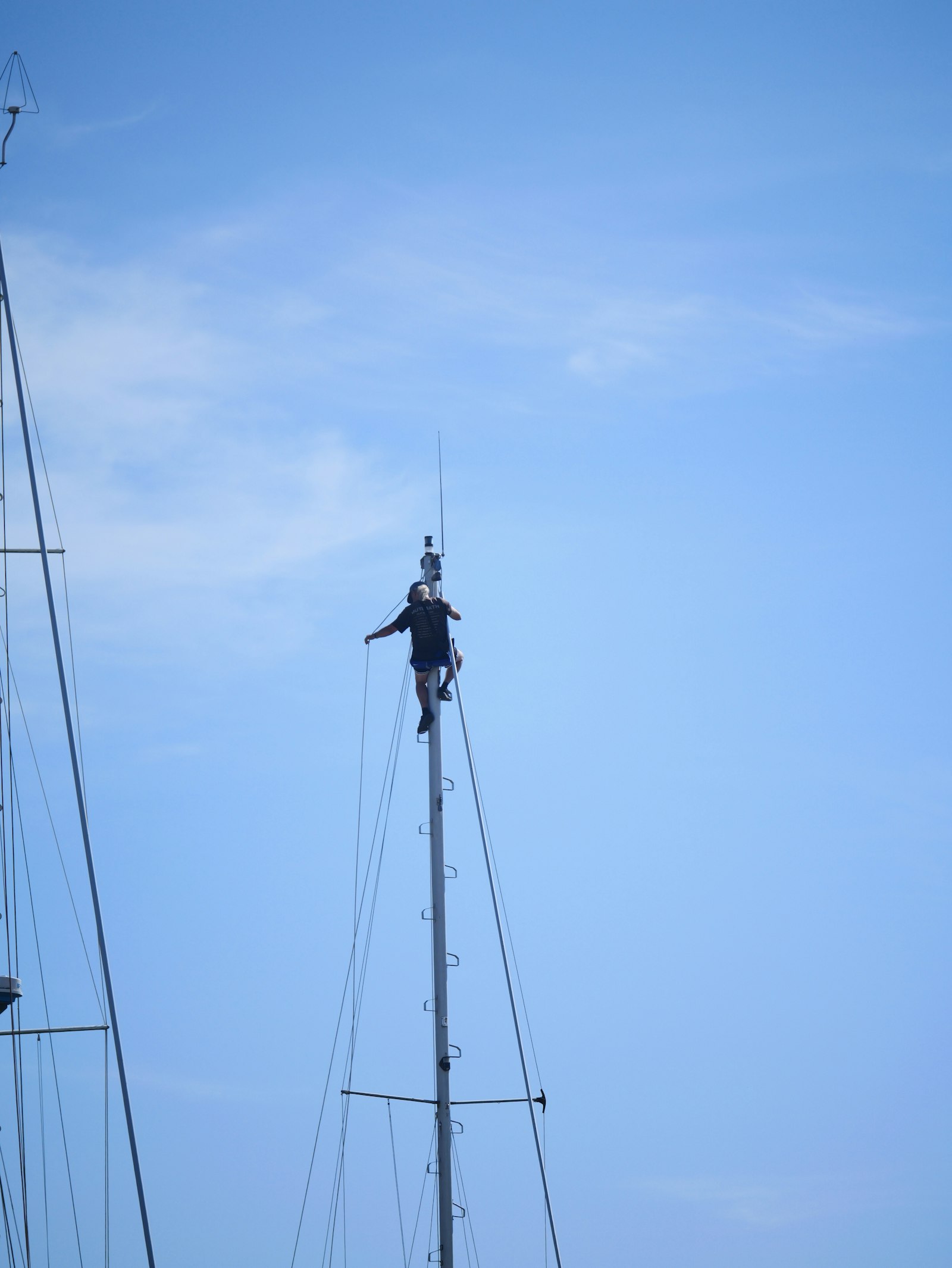 Rigger working aloft at the top of a sailing yacht mast